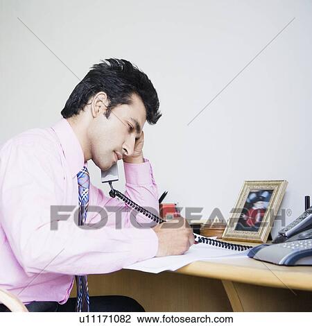 Side profile of a businessman talking on the telephone and writing on a paper View Large Photo Image Stock Image - Side profile of a businessman talking on the telephone and writing on a paper. Fotosearch