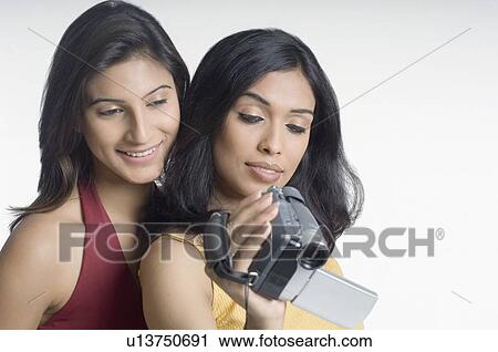 Stock Image - Close-up of a young woman holding a home video camera and another young woman looking at it. Fotosearch