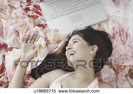 High angle view of a young woman lying on the bed with a laptop beside her View Large Photo Image Stock Photography - High angle view of a young woman lying on the bed with a laptop beside her. Fotosearch