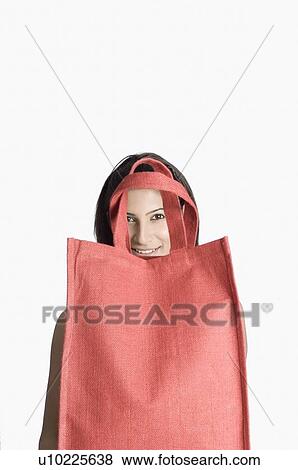 Portrait of a young woman looking through handle of a shopping bag View Large Photo Image Stock Photo - Portrait of a young woman looking through handle of a shopping bag. Fotosearch