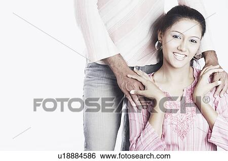 Portrait of a young woman smiling with a young man standing behind her View Large Photo Image Stock Photograph - Portrait of a young woman smiling with a young man standing behind her. Fotosearch