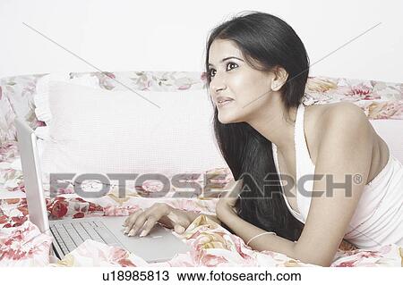 Side profile of a young woman lying on the bed using a laptop View Large Photo Image Stock Image - Side profile of a young woman lying on the bed using a laptop. Fotosearch