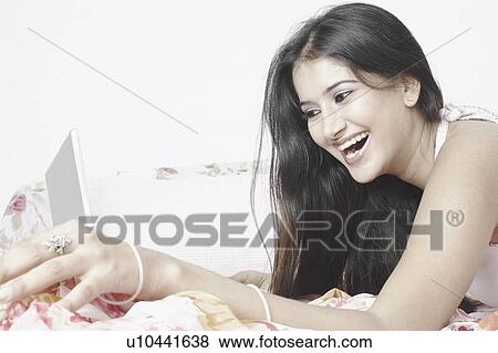Side profile of a young woman lying on the bed using a laptop View Large Photo Image Stock Photo - Side profile of a young woman lying on the bed using a laptop. Fotosearch