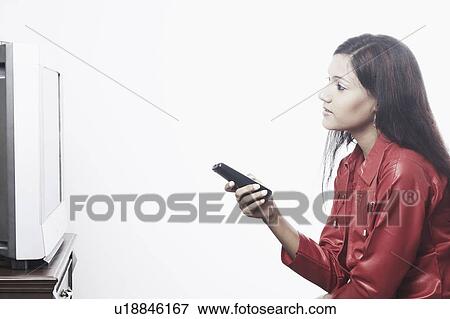 Side profile of a young woman watching television View Large Photo Image Stock Photo - Side profile of a young woman watching television. Fotosearch