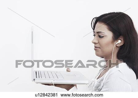 Side profile of a young woman wearing headphones holding a laptop View Large Photo Image Stock Image - Side profile of a young woman wearing headphones holding a laptop. Fotosearch