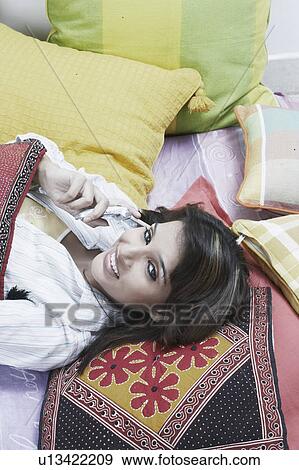 High angle view of a young woman lying down talking on a mobile phone View Large Photo Image Stock Photo - High angle view of a young woman lying down talking on a mobile phone. Fotosearch