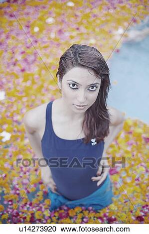 Stock Image - High angle view of a young woman standing in a swimming pool filled with flower petals. Fotosearch