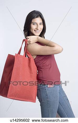 Portrait of a young woman carrying a shopping bag and smiling View Large Photo Image Stock Image - Portrait of a young woman carrying a shopping bag and smiling. Fotosearch