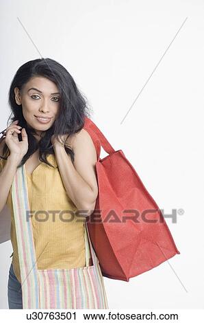 Portrait of a young woman carrying a shopping bag and smiling View Large Photo Image Stock Image - Portrait of a young woman carrying a shopping bag and smiling. Fotosearch