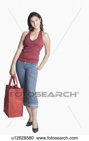 Stock Image - Portrait of a young woman holding a shopping bag and standing with her hand on her hip. Fotosearch
