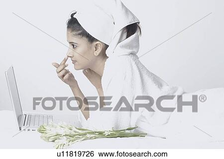 Stock Photograph - Side profile of a young woman lying in front of a laptop touching her nose. Fotosearch