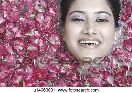 Stock Photo - High angle view of a young woman lying in a bathtub covered with flower petals. Fotosearch