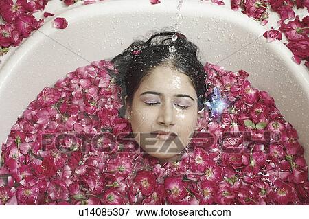 Stock Photo - High angle view of a young woman lying in a bathtub covered with flower petals. Fotosearch