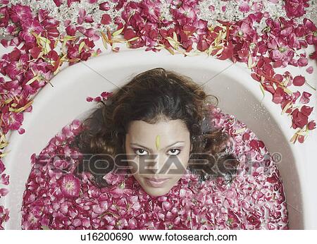 Stock Image - Portrait of a young woman lying in a bathtub with flower petals floating. Fotosearch