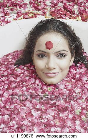Stock Photograph - Portrait of a young woman lying in a bathtub covered with flower petals. Fotosearch