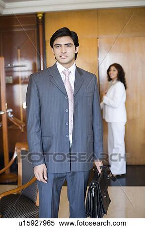 Stock Photography - Businessman holding a bag with a businesswoman standing in the background. Fotosearch