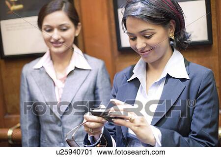 Stock Image - Businesswoman looking at a digital camera with another businesswoman standing beside her. Fotosearch