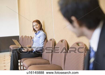 Stock Photo - Businesswoman using a laptop and looking at a businessman. Fotosearch