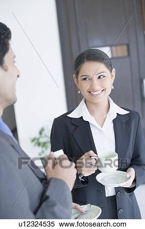 Stock Photography - Close-up of a businessman and a businesswoman holding cups of tea. Fotosearch