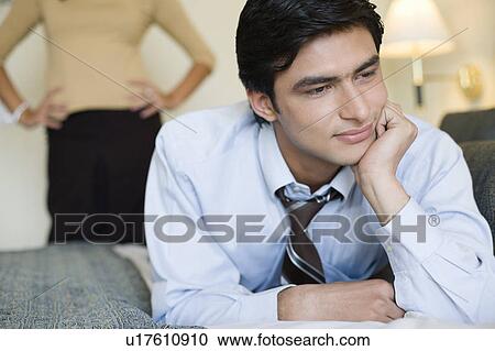 Close-up of a businessman lying on the bed with a young woman standing in the background View Large Photo Image Stock Image - Close-up of a businessman lying on the bed with a young woman standing in the background. Fotosearch
