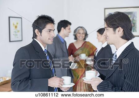Close-up of two businessmen holding cups of tea with their colleagues standing behind them View Large Photo Image Stock Image - Close-up of two businessmen holding cups of tea with their colleagues standing behind them. Fotosearch