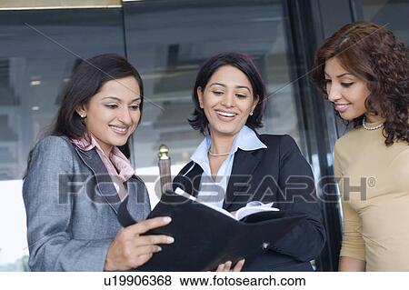 Low angle view of three businesswomen reading a diary and smiling View Large Photo Image Stock Photo - Low angle view of three businesswomen reading a diary and smiling. Fotosearch
