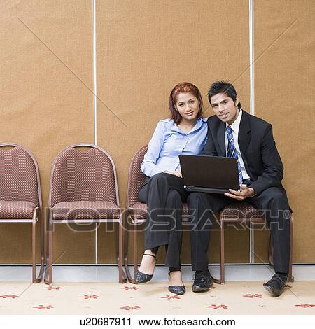 Portrait of a businessman and a businesswoman sitting on chairs with a laptop View Large Photo Image Stock Image - Portrait of a businessman and a businesswoman sitting on chairs with a laptop. Fotosearch