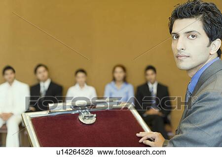 Portrait of a businessman at a lectern with his colleagues in the background View Large Photo Image Stock Photo - Portrait of a businessman at a lectern with his colleagues in the background. Fotosearch