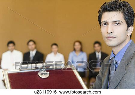 Stock Photograph - Portrait of a businessman at a lectern with his colleagues in the background. Fotosearch