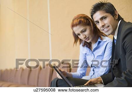 Portrait of a businessman sitting with a businesswoman and using a laptop View Large Photo Image Stock Photo - Portrait of a businessman sitting with a businesswoman and using a laptop. Fotosearch