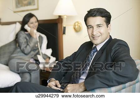 Stock Photo - Portrait of a businessman smiling with a businesswoman talking on the telephone in the background. Fotosearch