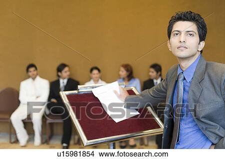 Portrait of a businessman standing at a lectern with his colleagues in the background View Large Photo Image Picture - Portrait of a businessman standing at a lectern with his colleagues in the background. Fotosearch