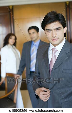 Stock Photograph - Portrait of a businessman with two business executives standing in the background. Fotosearch
