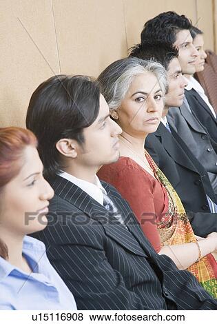 Stock Photo - Portrait of a businesswoman sitting between five business executives and looking serious. Fotosearch