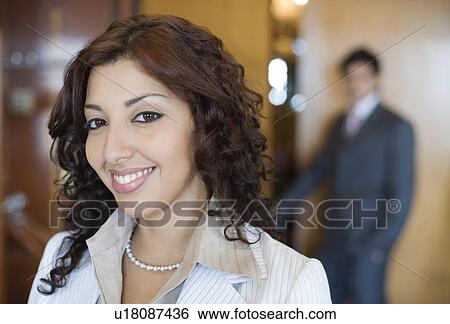 Portrait of a businesswoman smiling with a businessman standing in the background View Large Photo Image Stock Photograph - Portrait of a businesswoman smiling with a businessman standing in the background. Fotosearch
