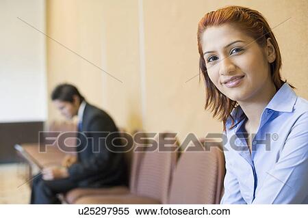 Stock Photography - Portrait of a businesswoman smiling with a businessman using a laptop in the background. Fotosearch