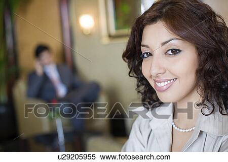 Stock Photography - Portrait of a businesswoman smiling with a businessman sitting in an armchair in the background. Fotosearch