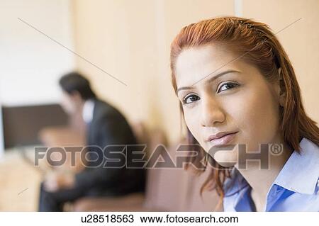 Stock Image - Portrait of a businesswoman with a businessman using a laptop in the background. Fotosearch