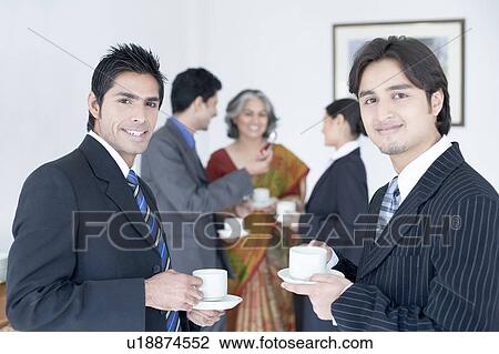 Portrait of two businessmen holding cups of tea with their colleagues standing behind them View Large Photo Image Stock Image - Portrait of two businessmen holding cups of tea with their colleagues standing behind them. Fotosearch
