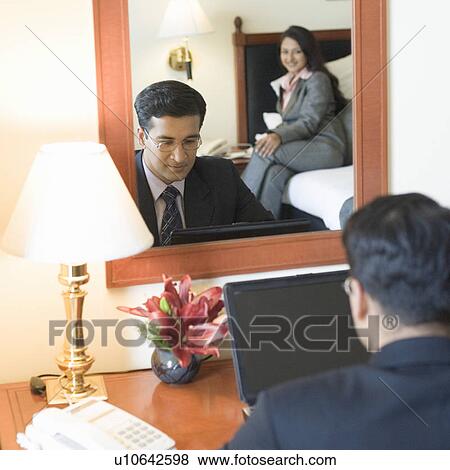Rear view of a businessman working on a laptop and reflection of a businesswoman sitting on the bed in a mirror View Large Photo Image Stock Photo - Rear view of a businessman working on a laptop and reflection of a businesswoman sitting on the bed in a mirror. Fotosearch