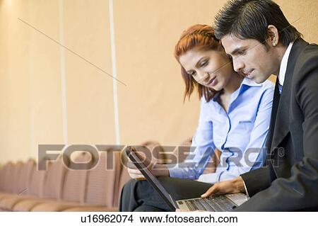 Side profile of a businessman sitting with a businesswoman and using a laptop View Large Photo Image Picture - Side profile of a businessman sitting with a businesswoman and using a laptop. Fotosearch