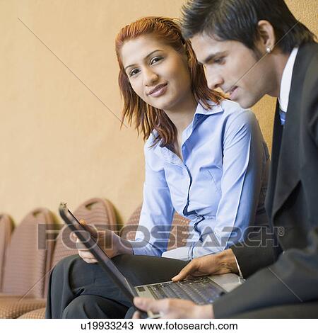 Stock Image - Side profile of a businessman using a laptop with a businesswoman sitting beside him. Fotosearch