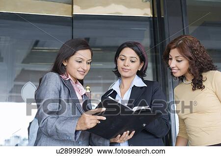 Three businesswomen standing together and looking at a file View Large Photo Image Stock Image - Three businesswomen standing together and looking at a file. Fotosearch