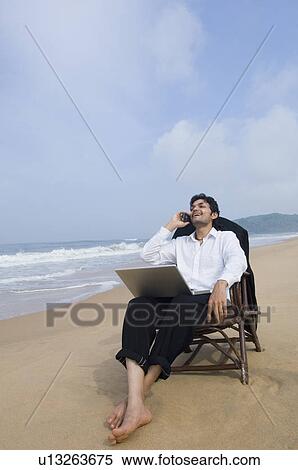 Businessman sitting in an armchair on the beach and talking on a mobile phone View Large Photo Image Stock Photography - Businessman sitting in an armchair on the beach and talking on a mobile phone. Fotosearch