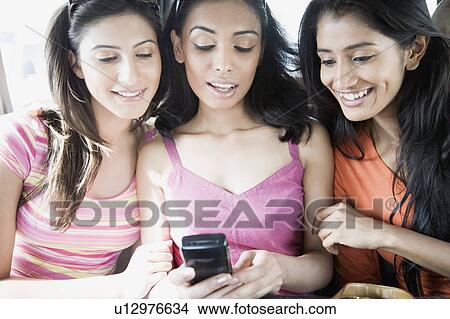 Picture - Close-up of three young women looking at a mobile phone and smiling. Fotosearch