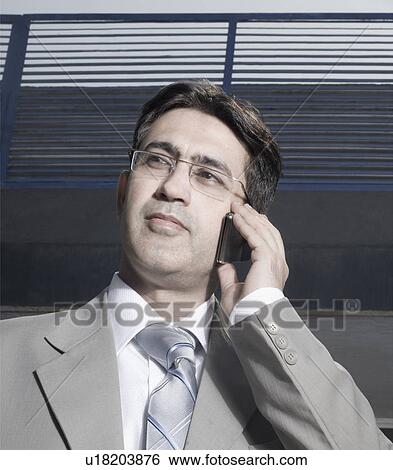Stock Photograph - Low angle view of a businessman talking on a mobile phone. Fotosearch