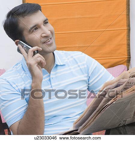 Mid adult man holding a newspaper and talking on a mobile phone View Large Photo Image Stock Photograph - Mid adult man holding a newspaper and talking on a mobile phone. Fotosearch