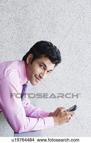 Picture - Portrait of a businessman holding a mobile phone and smiling. Fotosearch
