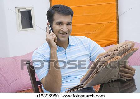 Stock Image - Portrait of a mid adult man talking on a mobile phone and holding a newspaper. Fotosearch