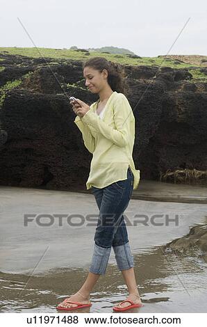 Side profile of a young woman text messaging and smirking on the beach View Large Photo Image Stock Photo - Side profile of a young woman text messaging and smirking on the beach. Fotosearch